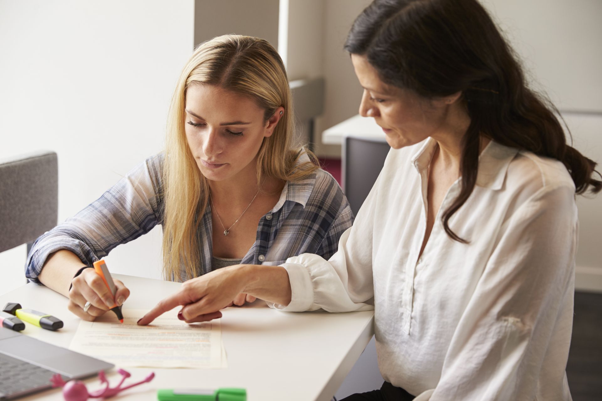 An instructor guides a student as she highlights text on a worksheet.