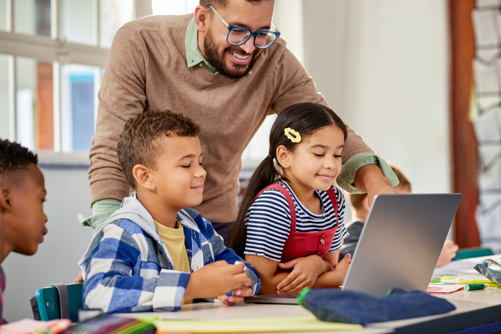 A teacher helps children work together on a laptop.