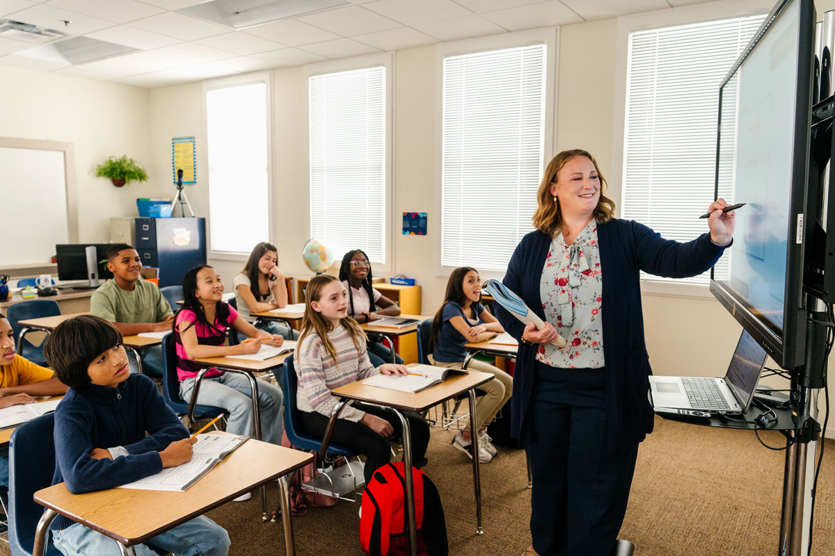 Teacher in front of classroom pointing at digital presentation