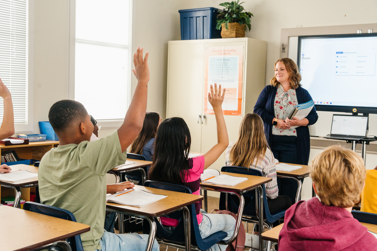 Teacher in front of classroom with hands raised
