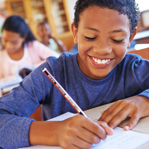 Student writing at desk and smiling