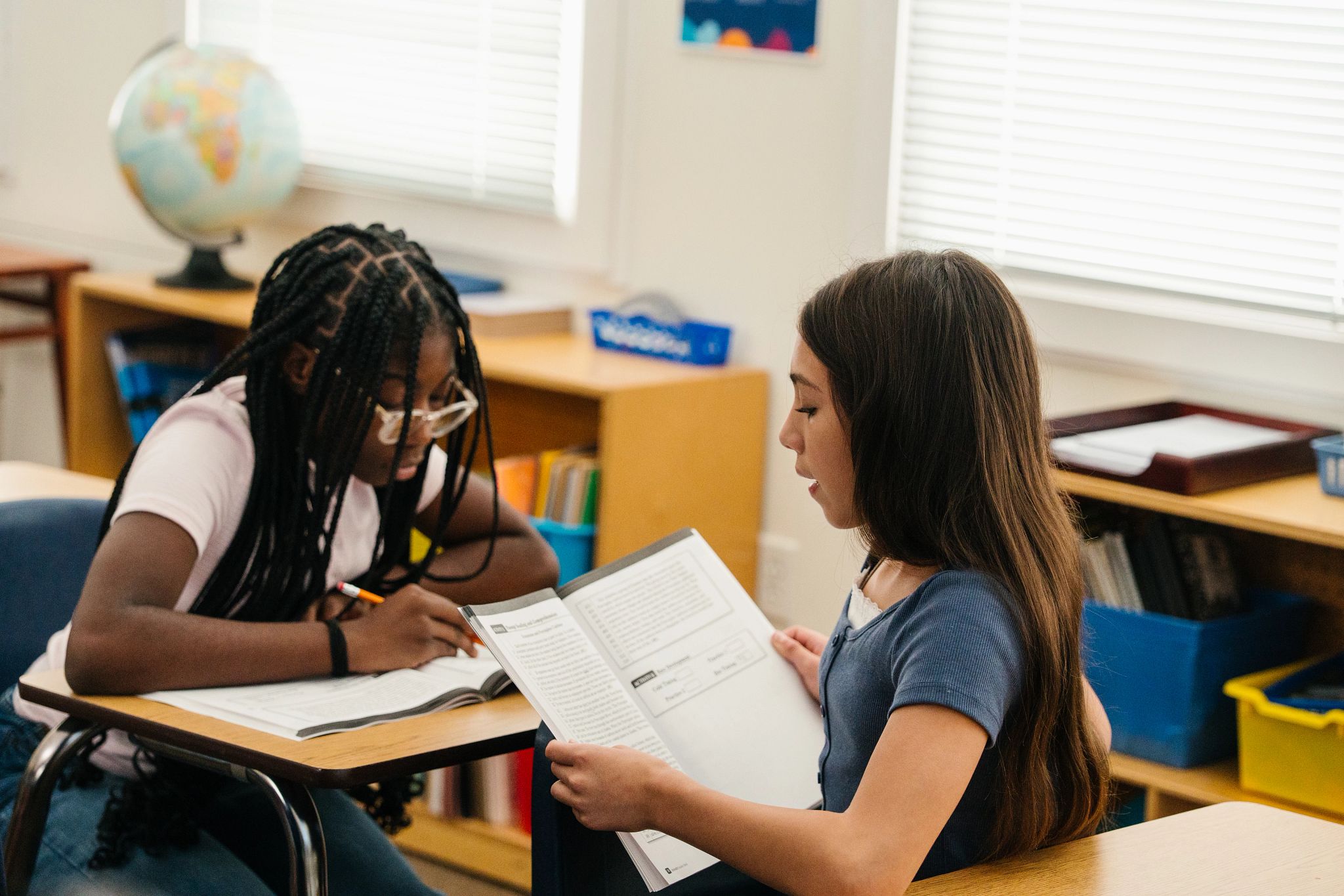 Two students engaged in a partner reading activity, such as one student reading aloud while the other follows along with a finger or pencil in a middle or high school classroom setting