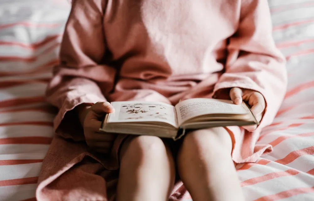 Child reading a book in bed